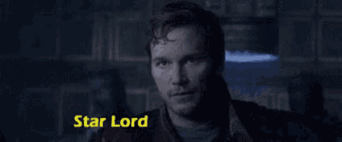 a man with a beard is standing in a dark room with the words star lord written on the bottom .