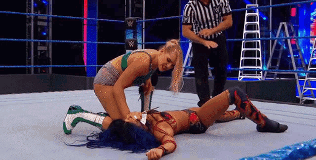 two women are wrestling in a wrestling ring and one of them is laying on the ground .