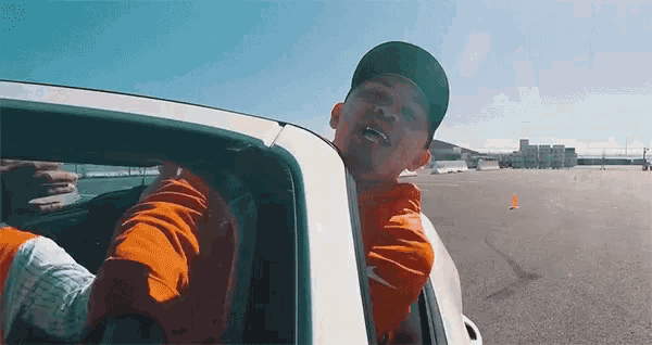 a man wearing a hat and an orange jacket is sitting in a car .
