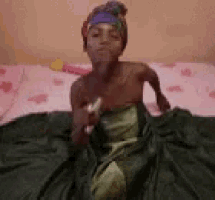 a woman in a green dress is sitting on a bed with a pink blanket .