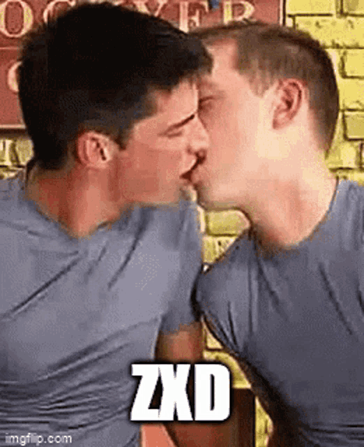 two men are kissing each other in front of a brick wall with the words zxd written on the bottom .