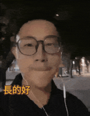 a man wearing glasses and ear buds is smiling with chinese writing behind him