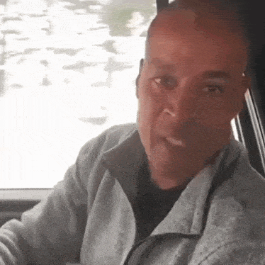 a man is sitting in the driver 's seat of a car smoking a cigarette .