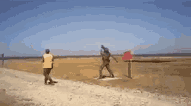 a man in a yellow vest is walking down a dirt road next to a man in a red vest