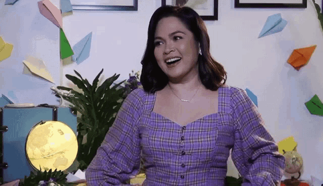 a woman in a purple plaid shirt is smiling in front of a wall with paper airplanes .