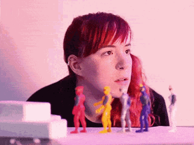 a woman with red hair and a nose ring is looking at a group of toy figures