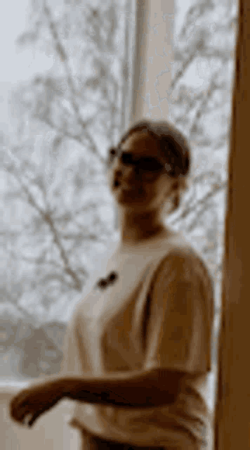 a woman is standing in front of a window wearing sunglasses .