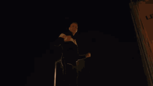 a man is standing in the dark with his fist in the air and a light behind him .