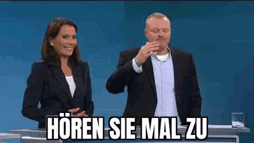 a man and a woman are standing next to each other in front of a blue background . the man is using sign language .