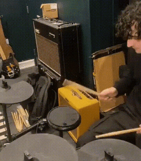 a man is playing drums in a room with a yellow amplifier behind him .