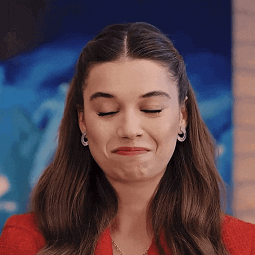 a woman wearing hoop earrings and a red shirt makes a funny face