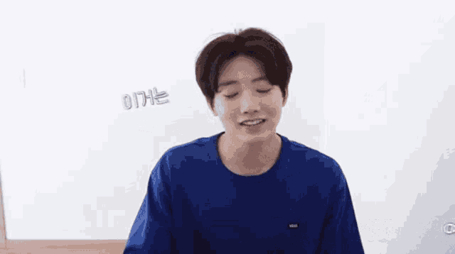 a young man in a blue shirt is smiling and looking at the camera with a foreign language written on the bottom right corner
