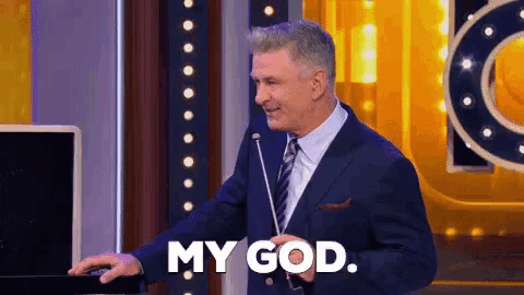 a man in a suit and tie holds a microphone and says my god