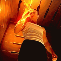 a man in a white tank top and black shorts is holding a fireball in his hand .