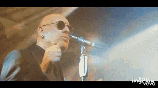 a bald man wearing sunglasses singing into a microphone
