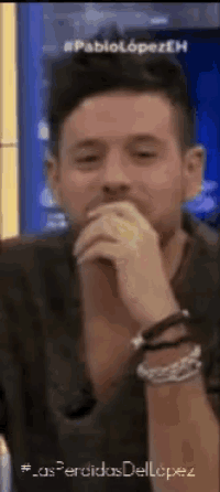 a man is covering his mouth with his hand while wearing bracelets on his wrists .