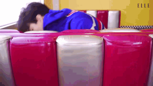 a man in a blue hoodie is sleeping on a red and white couch .