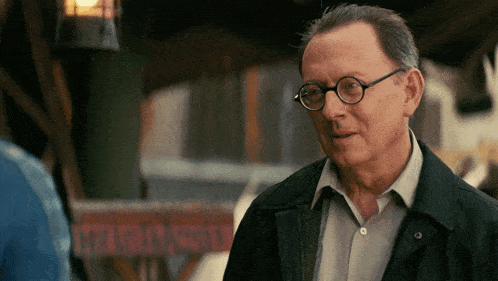 an older man wearing glasses and a black jacket stands in front of a sign that says " motel "