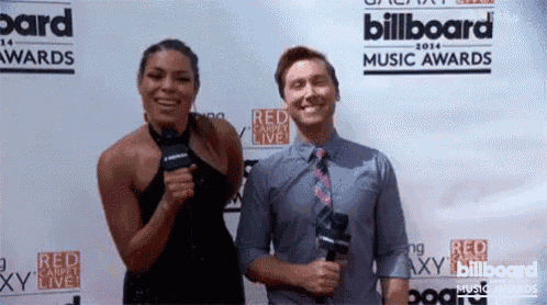 a man and a woman standing on a red carpet in front of a billboard