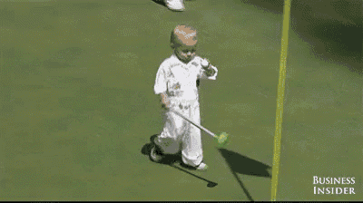 a little boy is playing golf on a green and the business insider is behind him