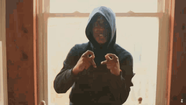 a man in a hooded sweatshirt is standing in front of a window and making a peace sign