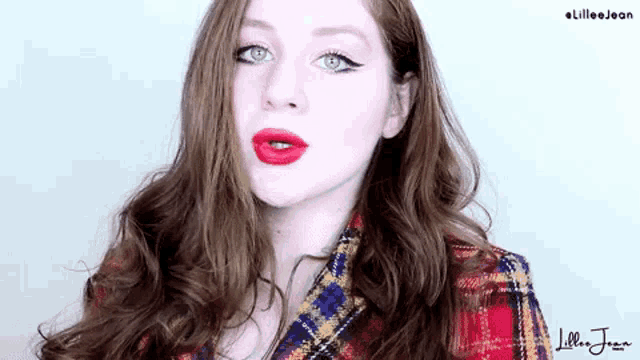a woman with red lipstick is wearing a plaid shirt and looking at the camera .