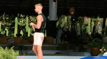a man in a black tank top and white shorts stands in front of a pool