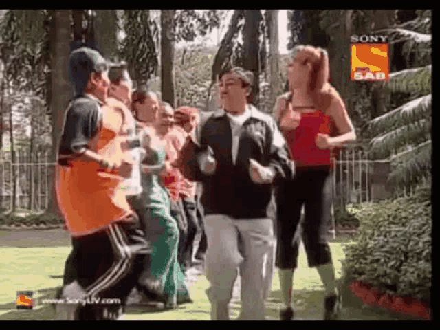 a group of people are dancing in a park in front of trees .