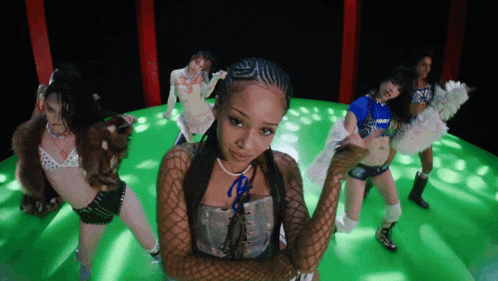 a group of women are dancing on a green stage and one of them is wearing a blue shirt that says army