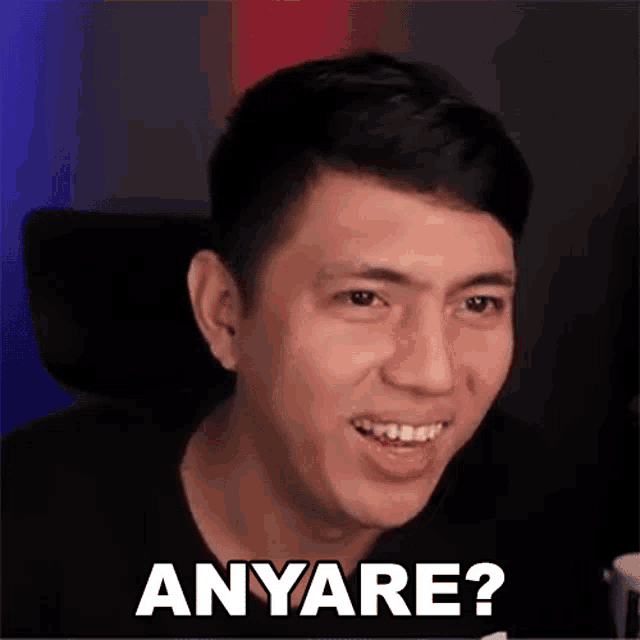 a man is smiling and making a funny face while sitting in a chair with the words anyare written on his face .