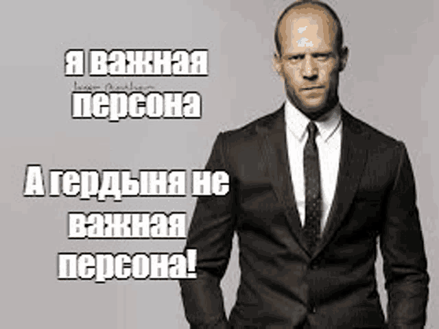 a man in a suit and tie is standing in front of a gray background with russian writing .