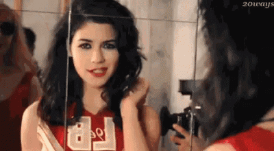a woman is looking at herself in a mirror while wearing a cheerleader uniform .