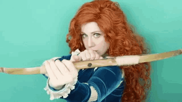 a woman with red hair is holding a wooden bow and arrow .