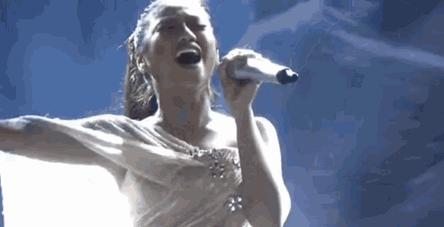 a woman is singing into a microphone while wearing a white dress .