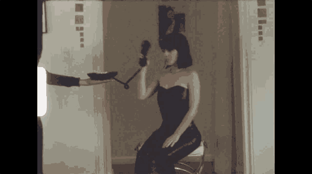 a woman in a black dress is sitting on a chair and holding a phone