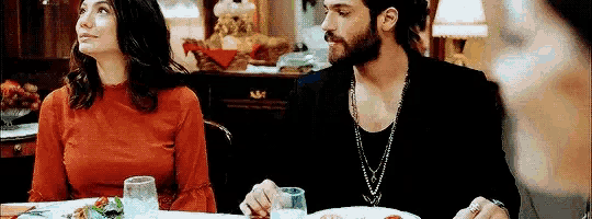a man and a woman are sitting at a table eating food and drinking wine .
