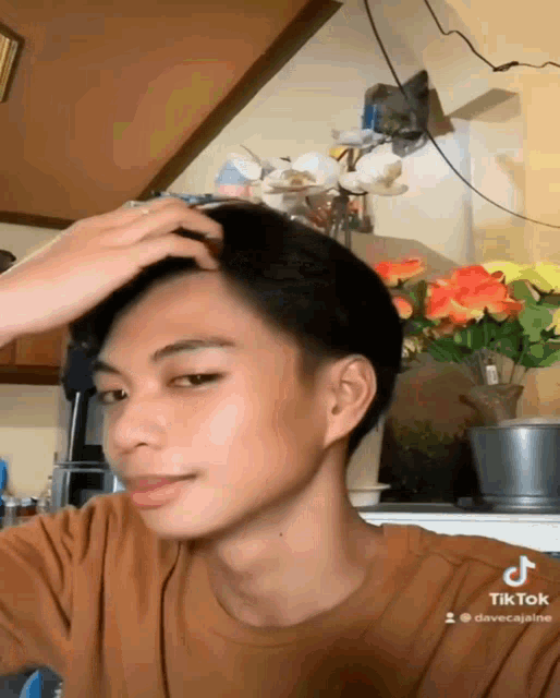 a young man adjusts his hair in front of a vase of flowers