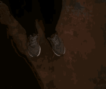 a person wearing a pair of gray sneakers and black pants is standing on a brown floor .