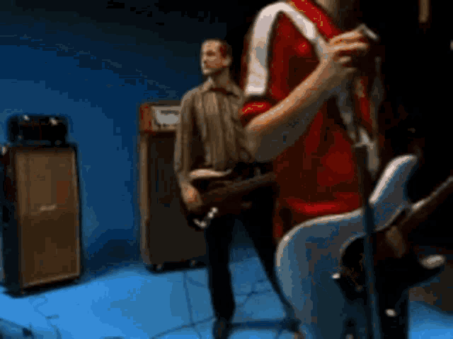 a man in a red shirt is playing a guitar in front of a marshall amplifier