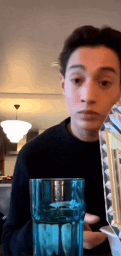 a young man is sitting at a table with a blue glass of water in front of him .