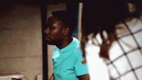 a man in a blue shirt is standing in a dark room with a fence in the background .