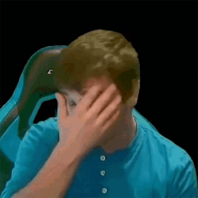 a man is covering his face with his hand while sitting in a chair .