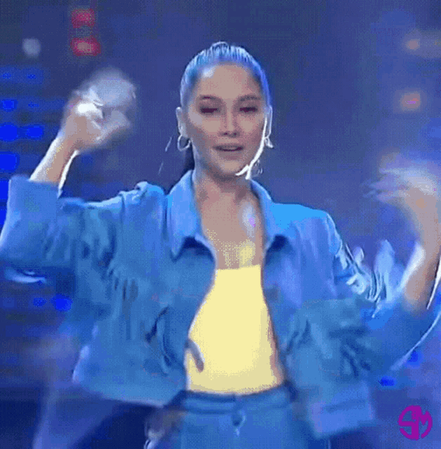 a woman wearing a blue jacket and yellow top is dancing on a stage