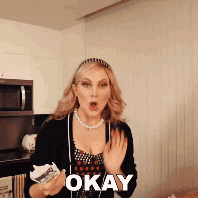 a woman in a kitchen holds a piece of paper and says " okay "