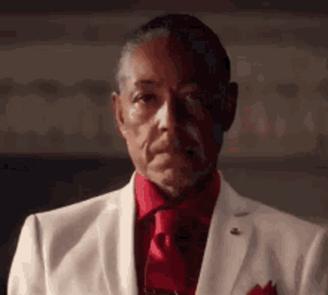 a man in a white suit and red tie is making a face .