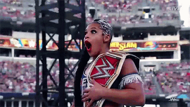 a woman is holding a wrestling championship belt in front of a crowd and a sign that says live