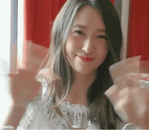a woman in a white top is smiling and waving at the camera