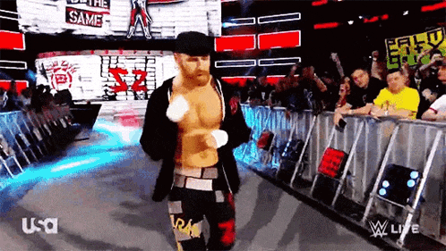 a wrestler is walking out of a ring with a crowd behind him and a sign that says the same on it .