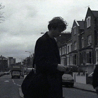 a black and white photo of a man walking down a street with a red truck that says barking on it