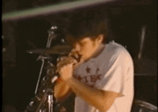 a man in a white shirt is playing drums and singing into a microphone on a stage .